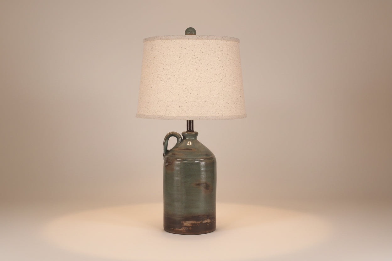Table lamp with a rustic green ceramic base and beige lampshade on a white background