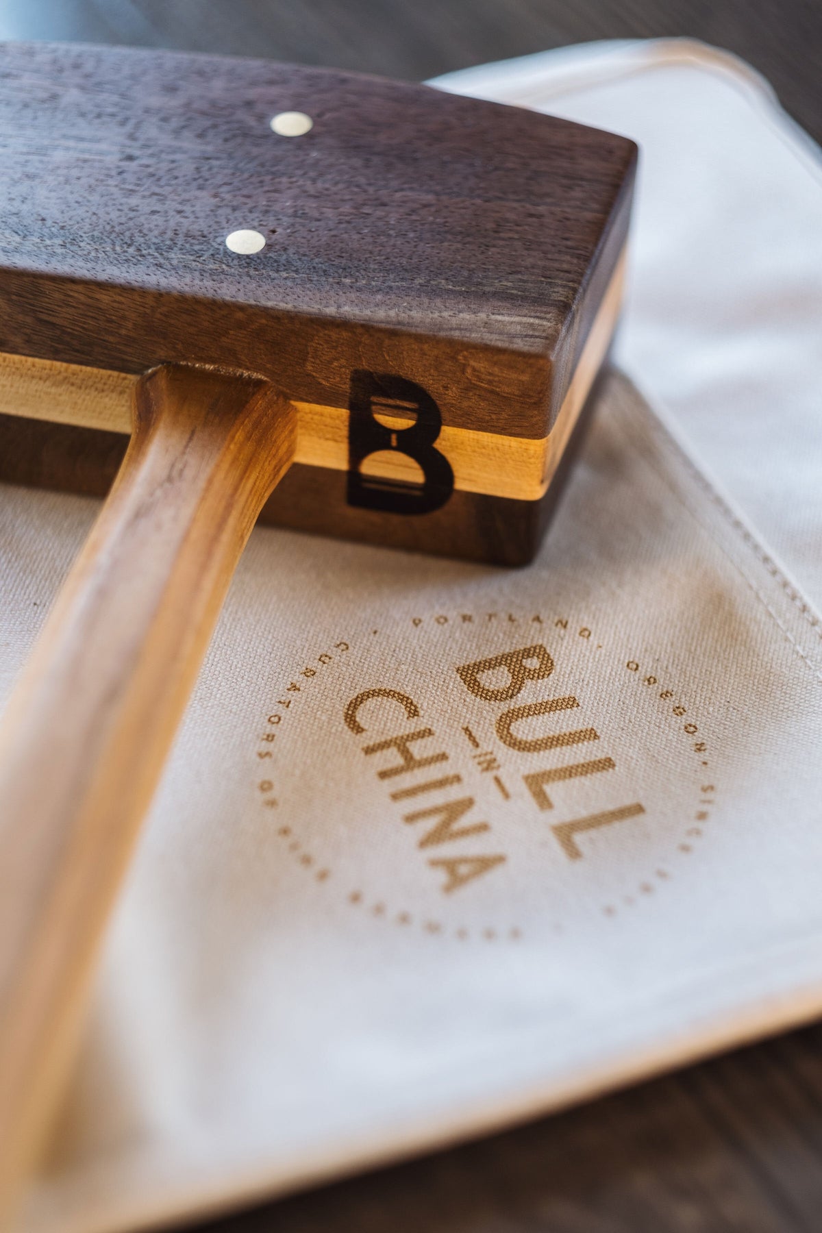 Diamond W Ranch black walnut ice mallet head close-up showing the B logo, resting on a Bull In China canvas bag