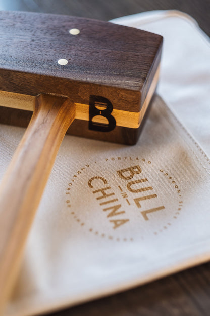 Diamond W Ranch black walnut ice mallet head close-up showing the B logo, resting on a Bull In China canvas bag