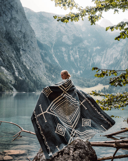 girl wearing achuar blanket standing on the shore of a lake with large, snowy mountains in the background