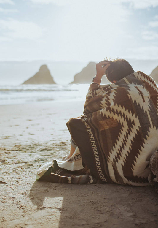 man sitting on beach with blanket on shoulders